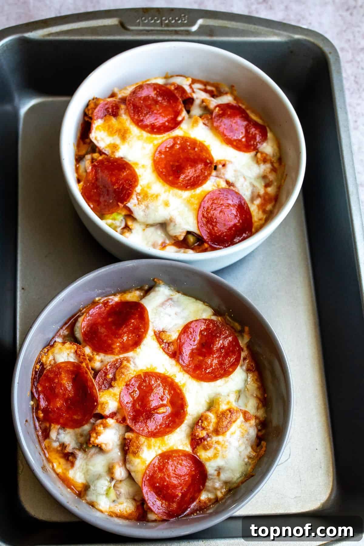 Baking sheet with pizza bowls in them and pepperoni on top.