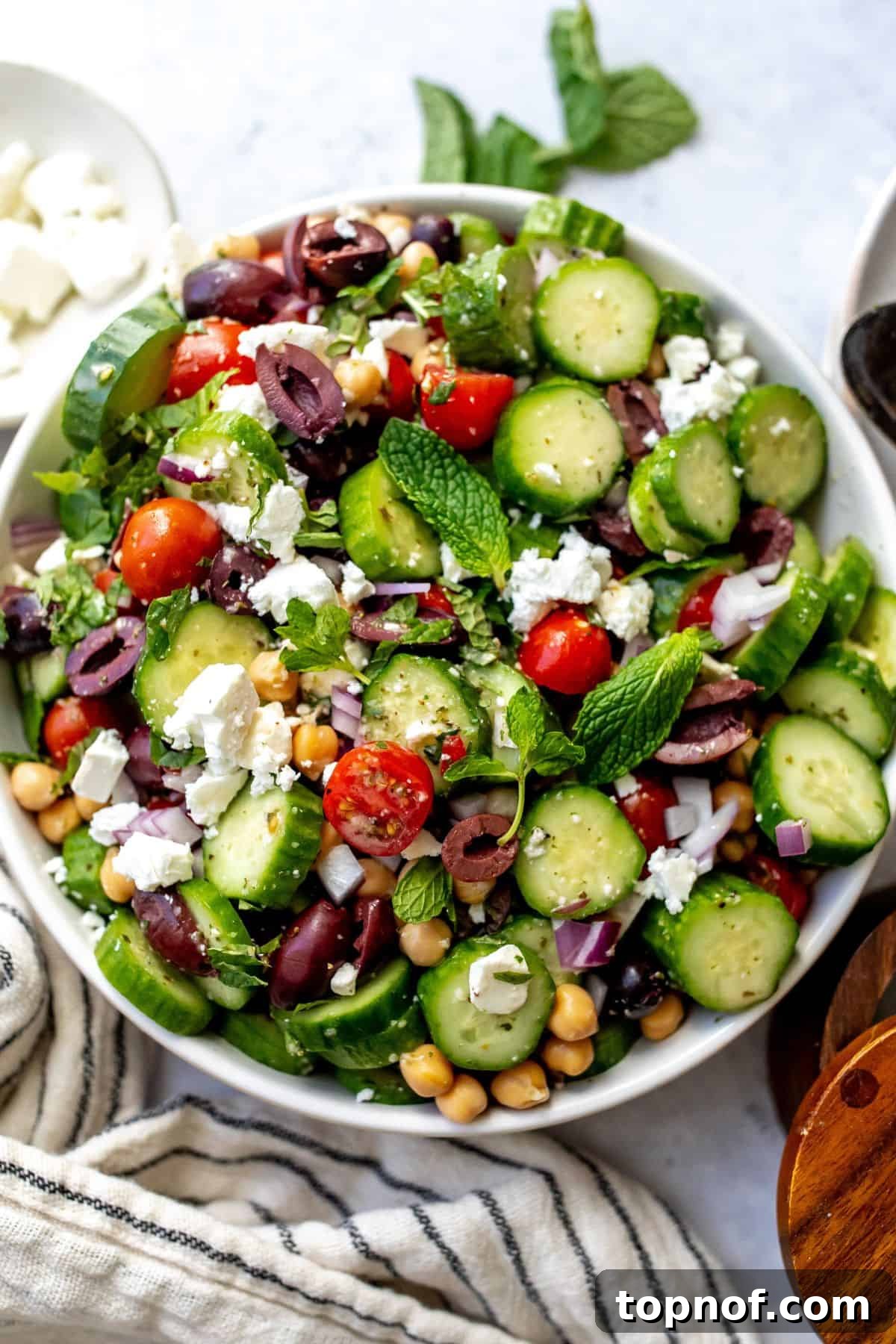 Mediterranean Cucumber Delight 2 Large white bowl with Greek cucumber salad and silver serving utensils on the side, highlighting its freshness and vibrant colors.