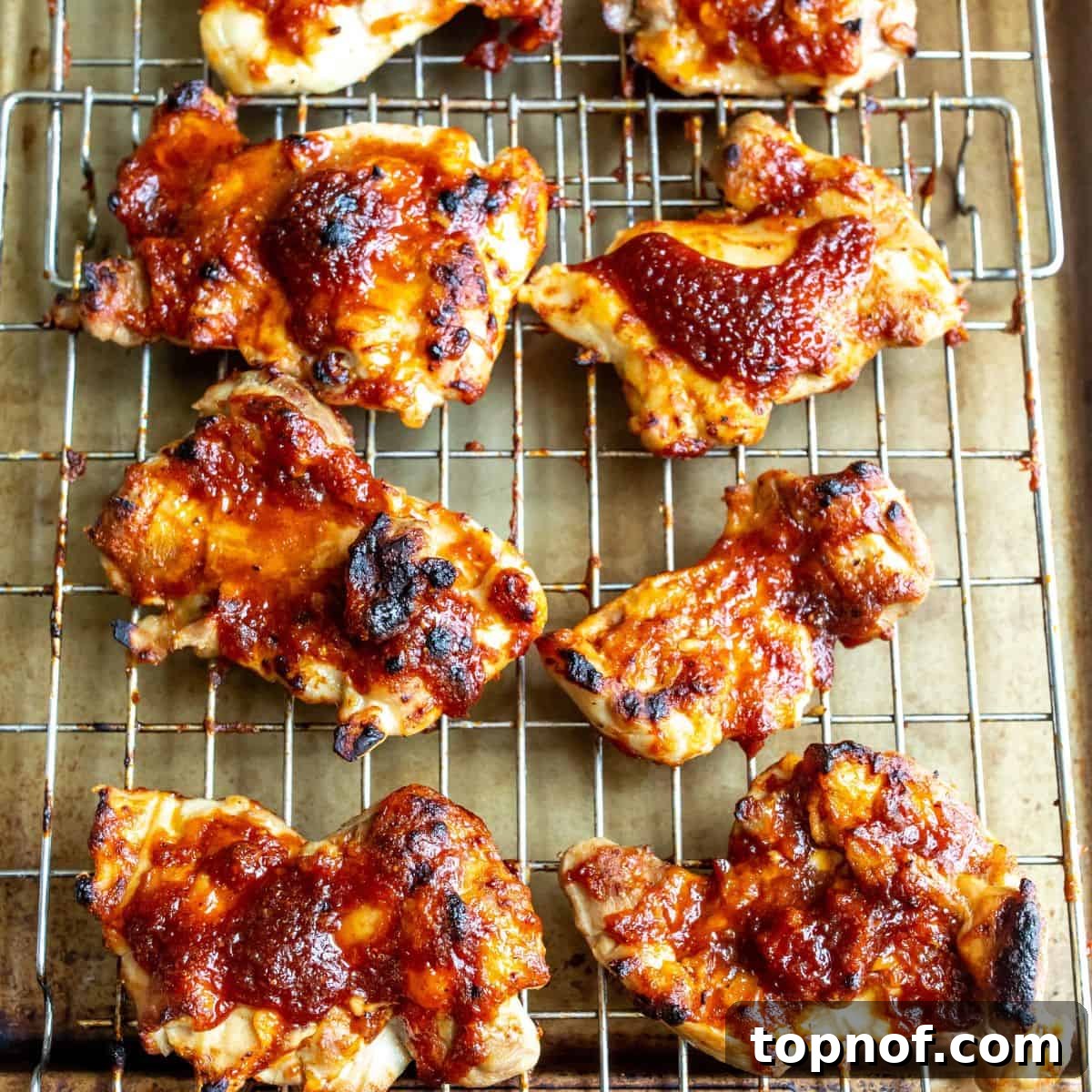 Glazed BBQ Chicken Thighs 5 BBQ chicken thighs arranged on a wire rack over a parchment-lined baking tray, halfway through cooking.