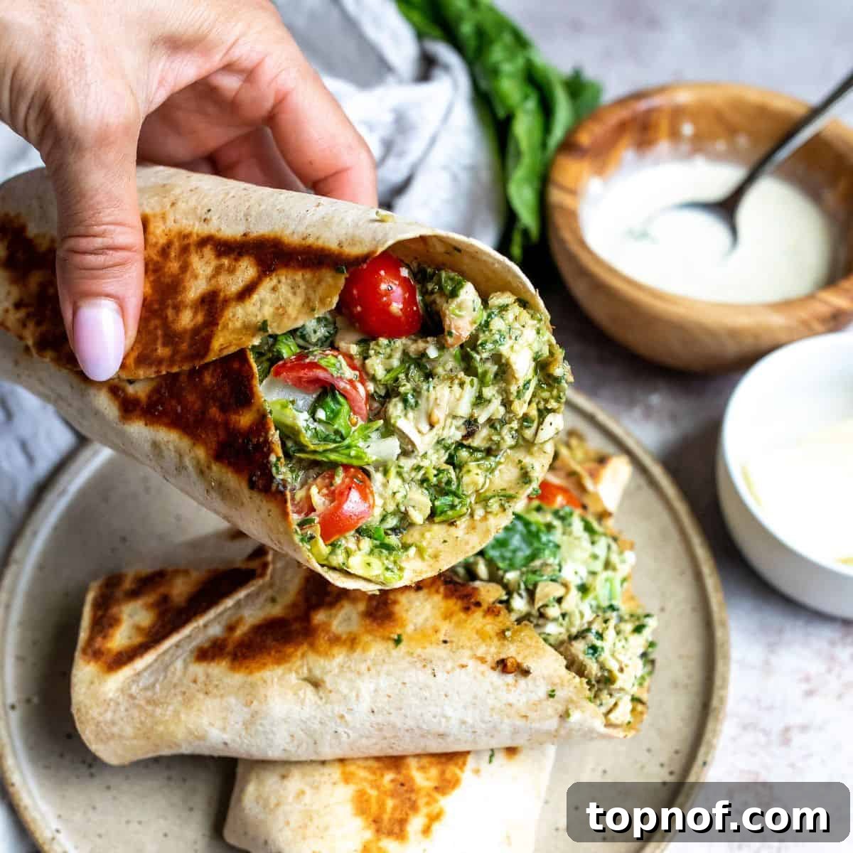 Vibrant Pesto Chicken Wraps 7 A hand holding a perfectly folded Pesto Chicken Wrap, with a side of extra pesto dressing for dipping, highlighting the delicious and satisfying meal.