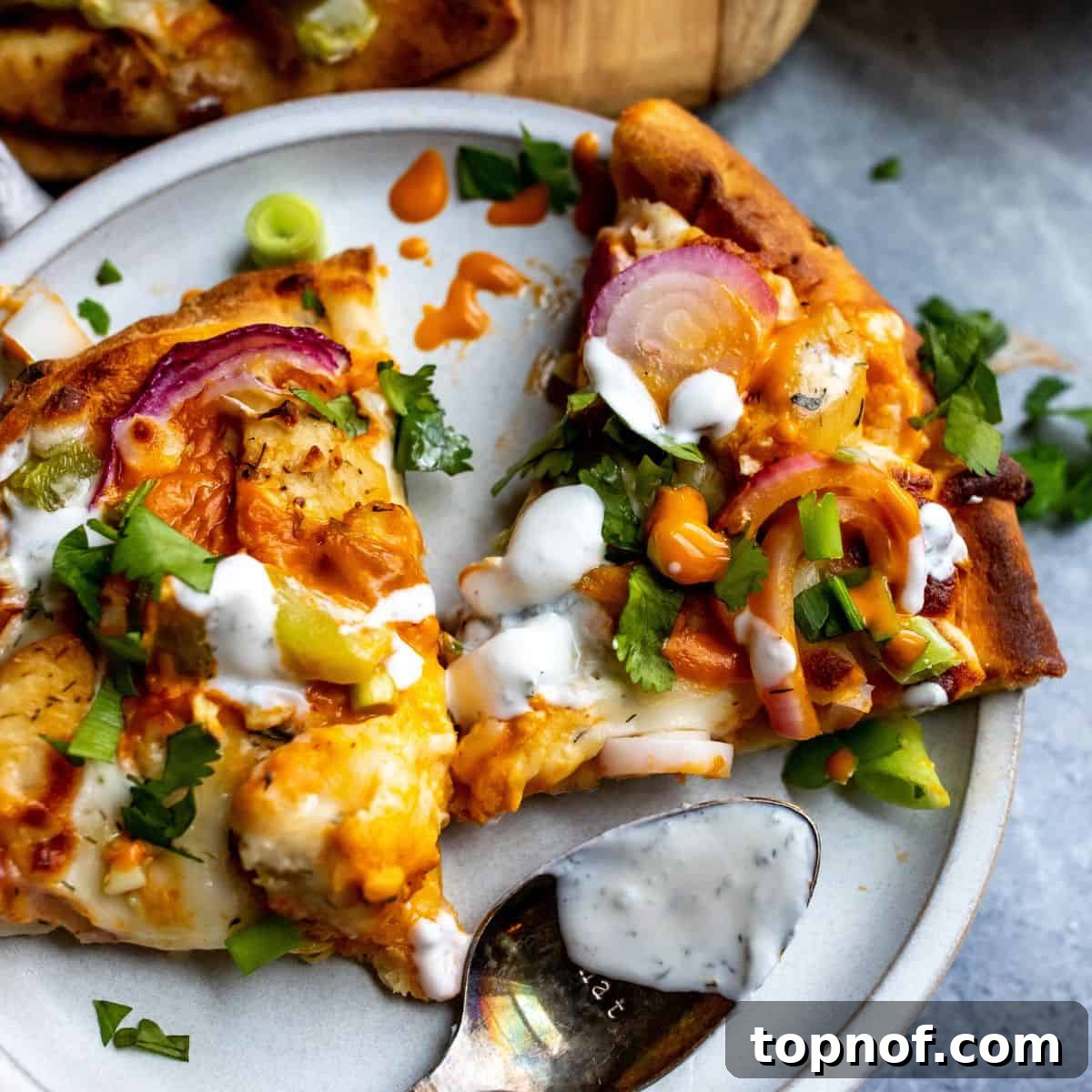 Signature Buffalo Chicken Flatbread 5 Up close photo of two slices of buffalo chicken flatbread on a white plate, garnished with green onions and ranch drizzle.