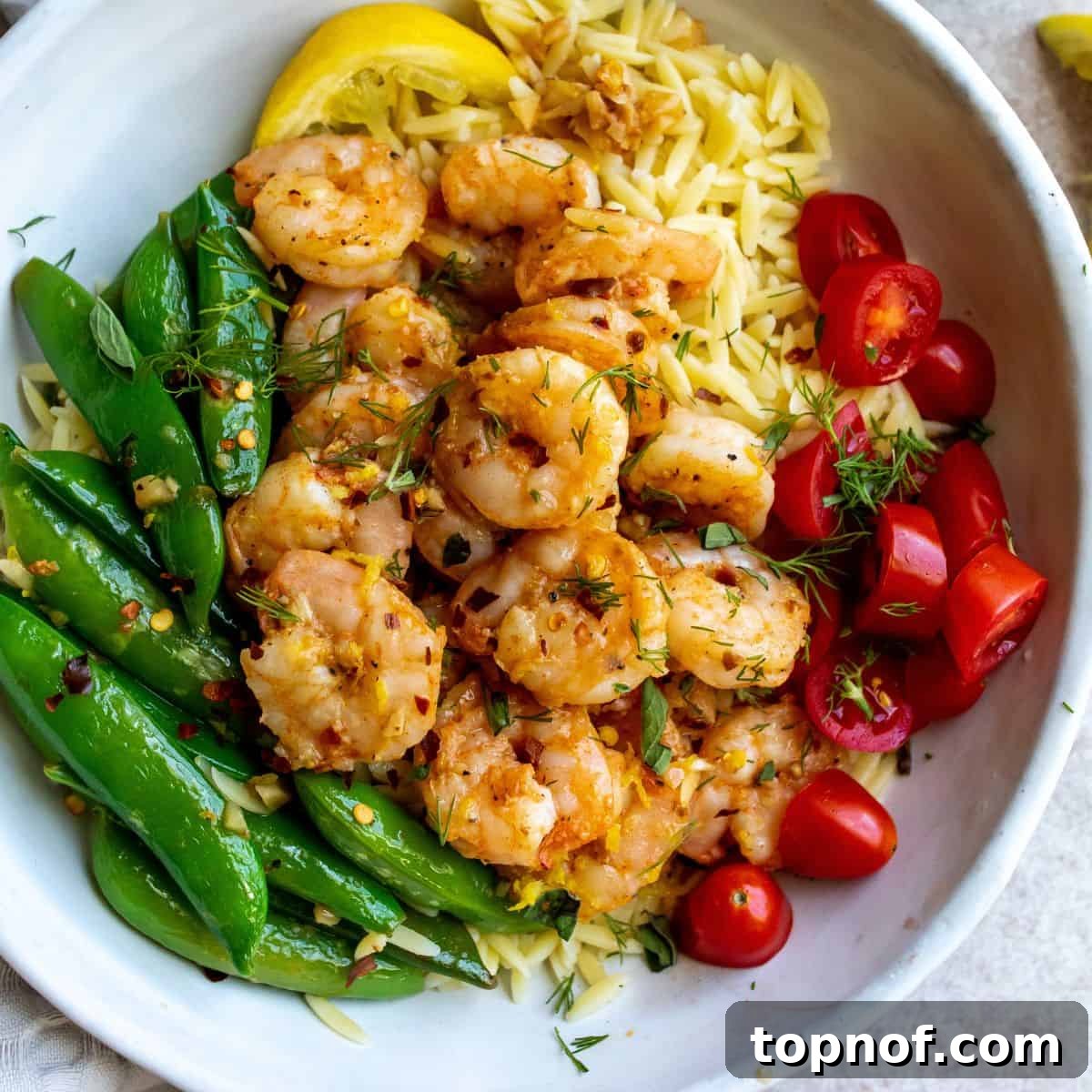Zesty Lemon Pepper Shrimp 6 A beautifully plated bowl of lemon pepper shrimp, orzo, cherry tomatoes, and snap peas, garnished with fresh herbs, ready to be eaten.
