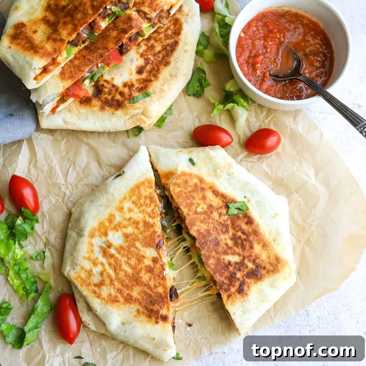 Two halves of a delicious homemade black bean crunchwrap supreme on parchment paper, ready to eat.