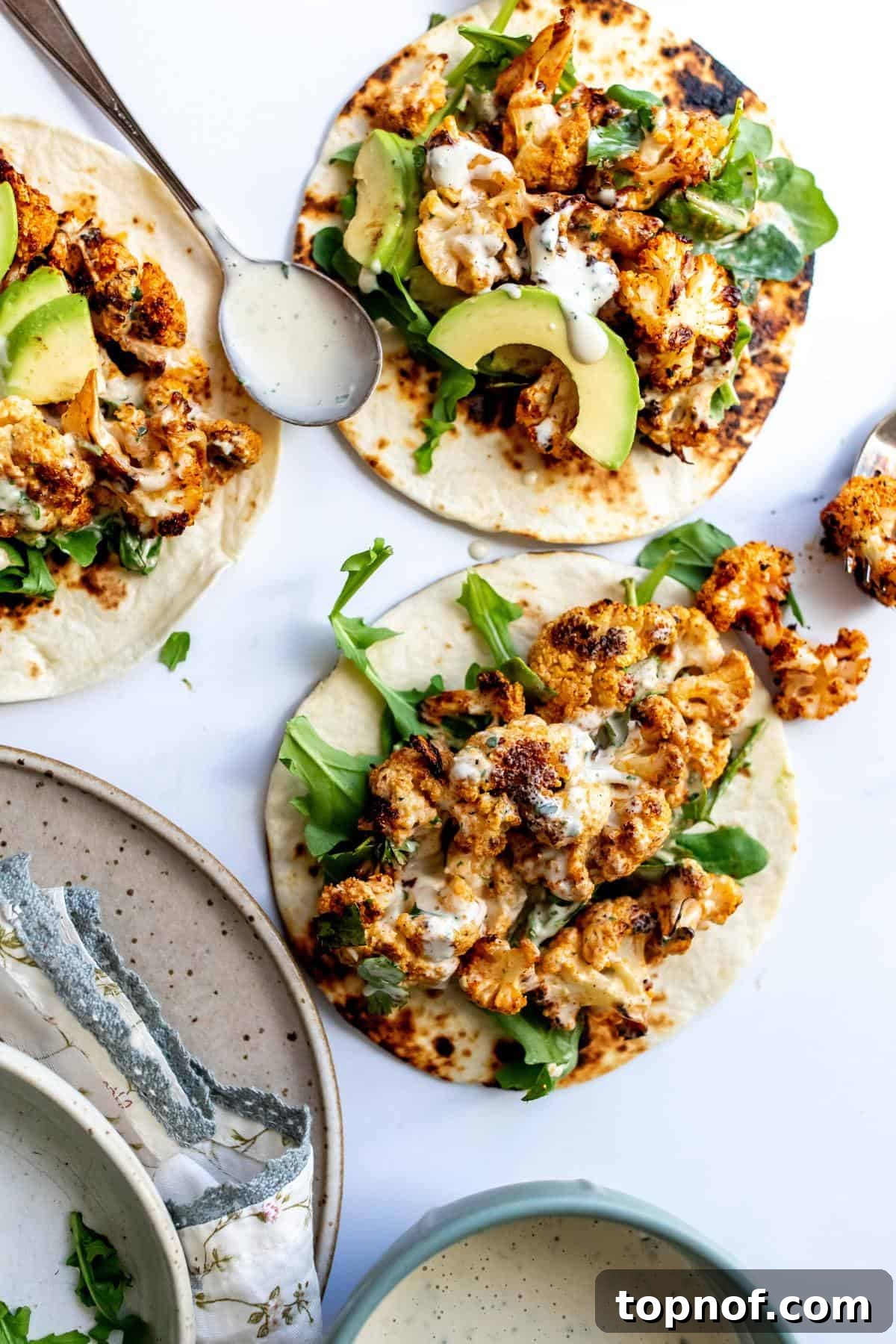 Crispy roasted cauliflower tacos generously drizzled with a rich smoky garlic sauce, presented beautifully on a white kitchen counter.
