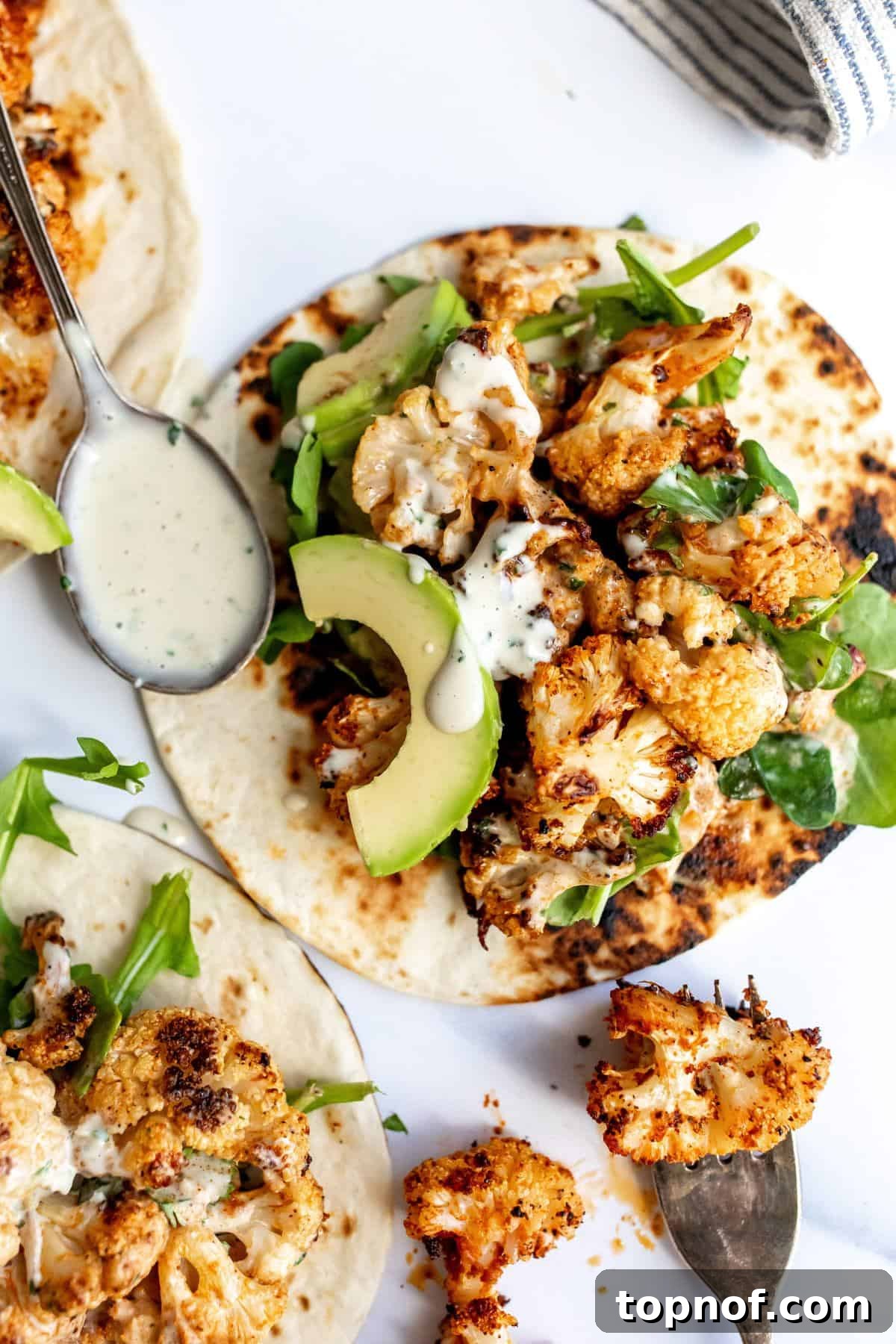 Close-up of fully assembled roasted cauliflower tacos with smoky sauce, fresh cilantro, and lime wedges on a white surface, ready to be enjoyed.