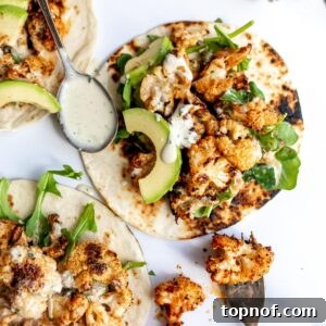 Roasted cauliflower tacos with a smoky sauce on a white counter with a spoon on the side.
