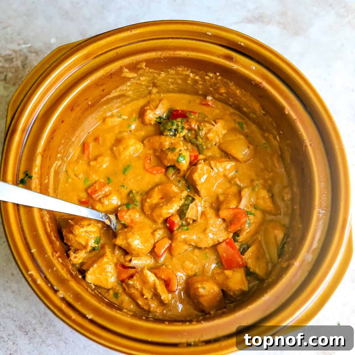Creamy Slow Cooker Satay Chicken 5 A brown slow cooker filled with perfectly cooked chicken satay, infused with colorful bell peppers and rich, creamy peanut sauce, ready to be served.