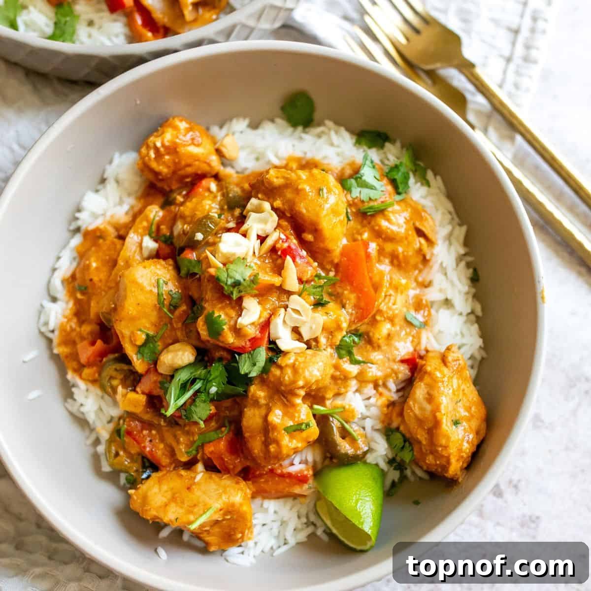 Creamy Slow Cooker Satay Chicken 6 A rustic gray ceramic bowl brimming with perfectly cooked slow cooker chicken satay served over fluffy rice, beautifully garnished, and accompanied by elegant gold forks, inviting you to savor every bite.