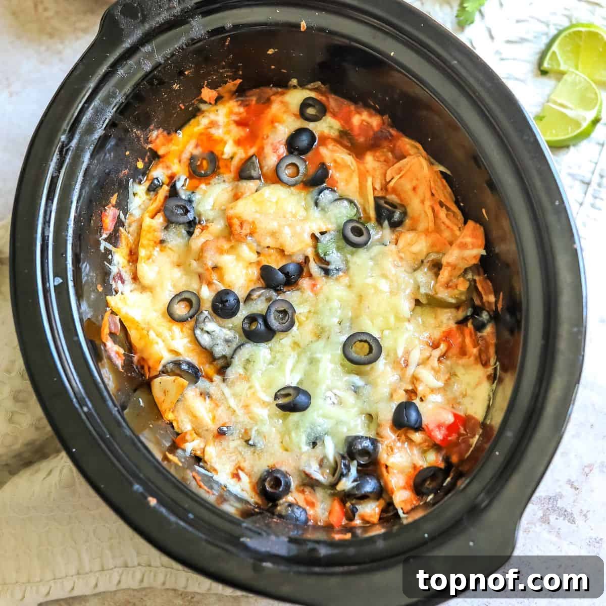 Melt-In-Your-Mouth Slow Cooker Chicken Enchiladas 6 Black slow cooker with melted cheese and olives.