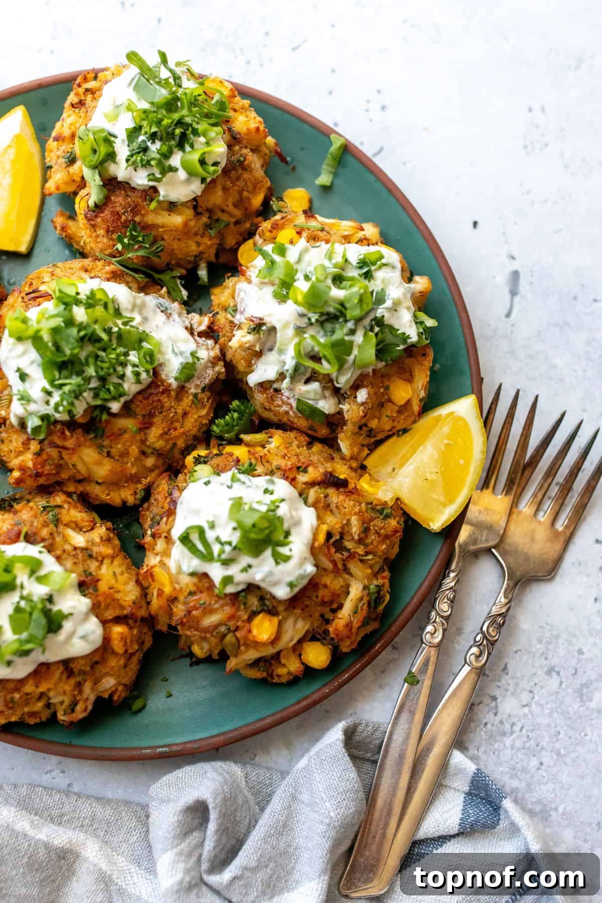 Maryland's Signature Crab Cakes 2 Perfectly golden Maryland Crab Cakes served on a green ceramic plate, garnished with fresh lemon wedges and ready to be enjoyed with two forks.
