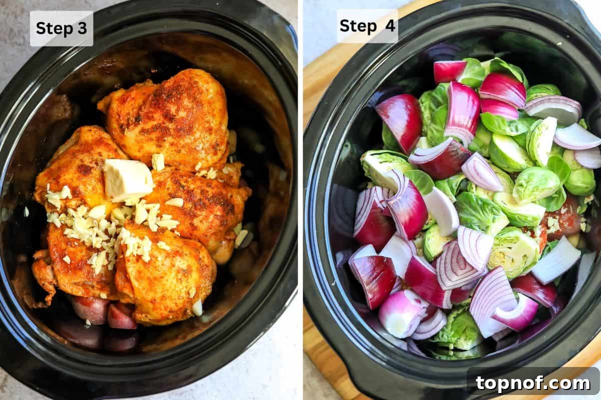A black slow cooker with layered ingredients: potatoes at the bottom, topped with seared chicken thighs, garlic, and butter.