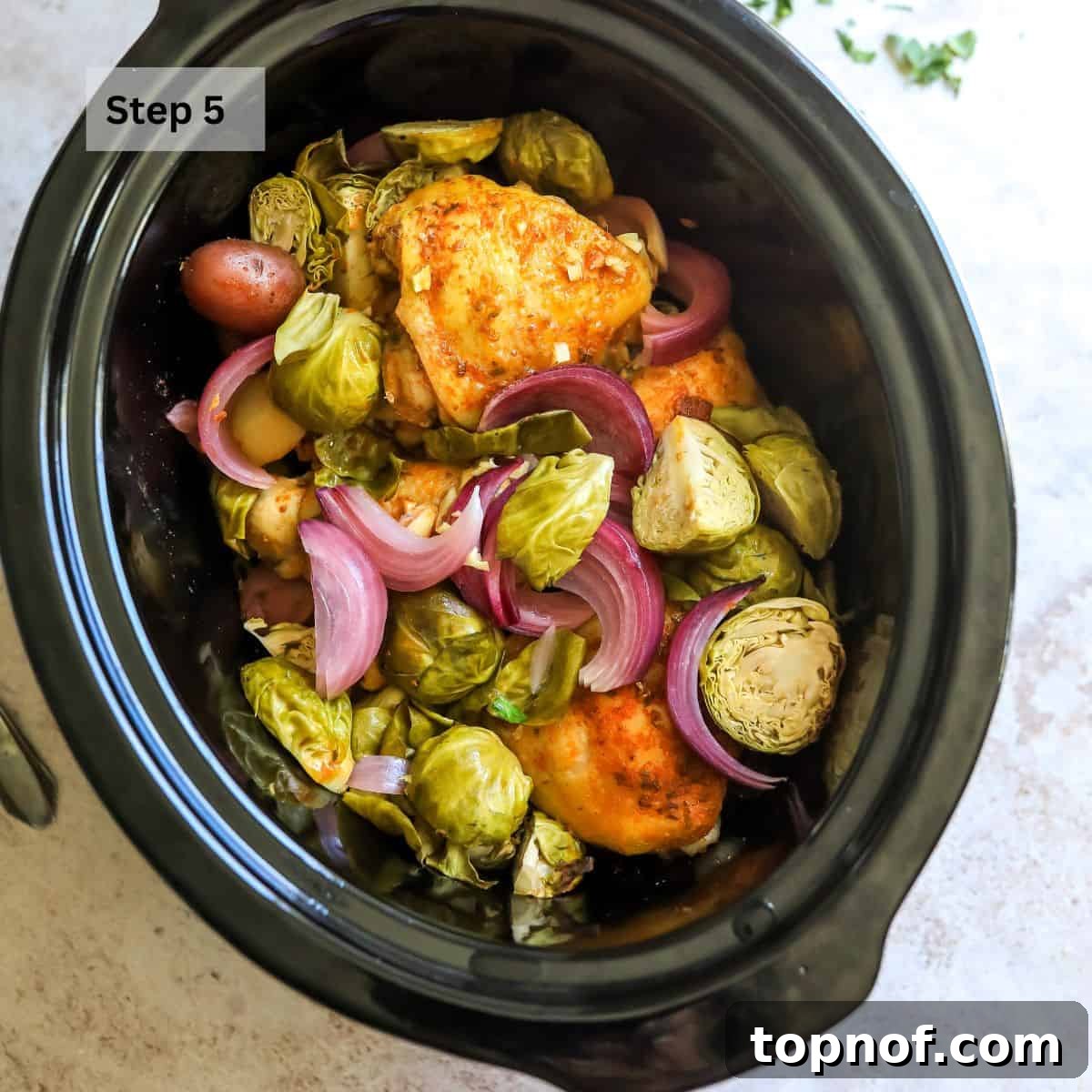 A close-up view of the slow cooker interior, showing perfectly cooked chicken, tender vegetables, and melted Parmesan cheese.