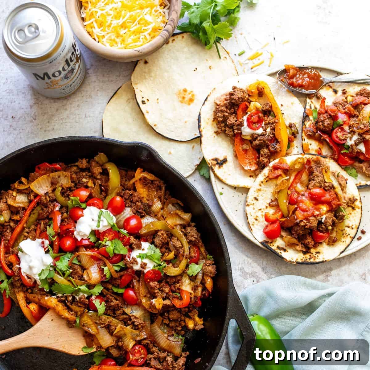 One-Pan Ground Beef Fajitas 2 Large black skillet with sizzling ground beef fajita mix, vibrant bell peppers and onions, topped with a dollop of sour cream and fresh cilantro, with warm tortillas neatly stacked on the side.