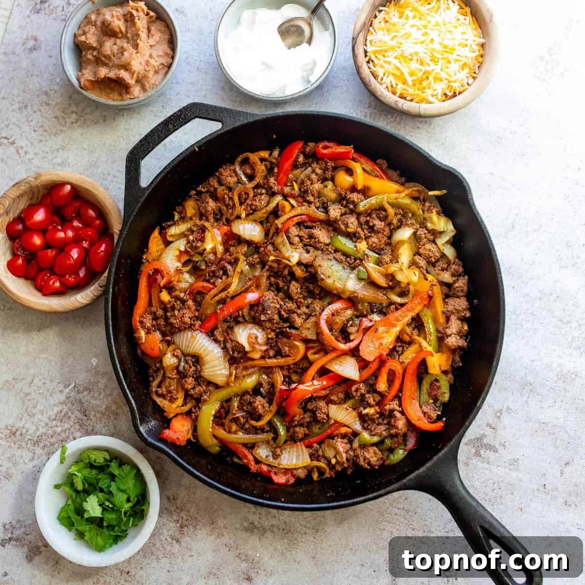 One-Pan Ground Beef Fajitas 5 Large black skillet filled with vibrant ground beef fajita mix, garnished with fresh cilantro, surrounded by small bowls of toppings including sour cream, cheese, diced tomatoes, and warm tortillas.