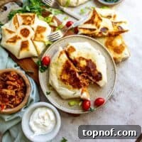 Tortillas stuffed with chicken and toppings on a ceramic plate with a fork on the side.