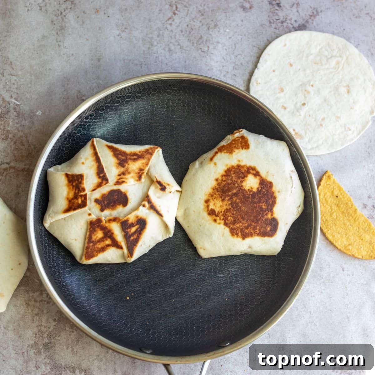 Ultimate Crispy Chicken Wrap 6 A black skillet on a stovetop with two perfectly toasted, golden-brown crunch wraps cooking, showing their crispy exterior.