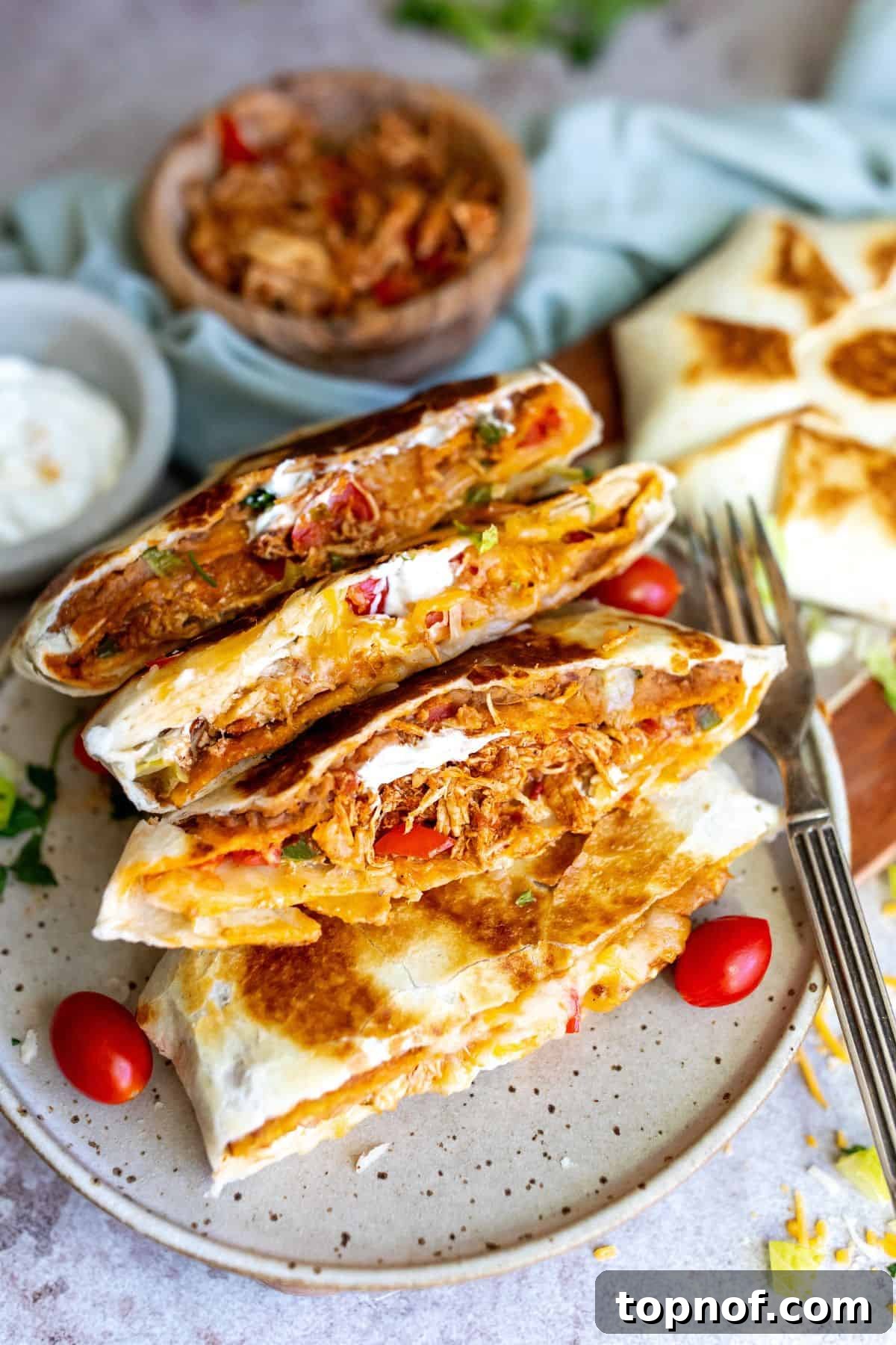 Ultimate Crispy Chicken Wrap 7 A hand holding a perfectly cooked Chicken Crunch Wrap Supreme, sliced open to reveal the delicious layers, with another wrap on a plate in the background.