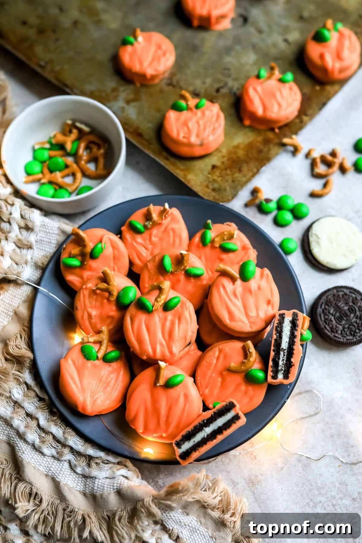 Adorable pumpkin-looking cookies arranged on a grey plate with a dish towel and soft lights in the background, showcasing a perfect fall aesthetic.