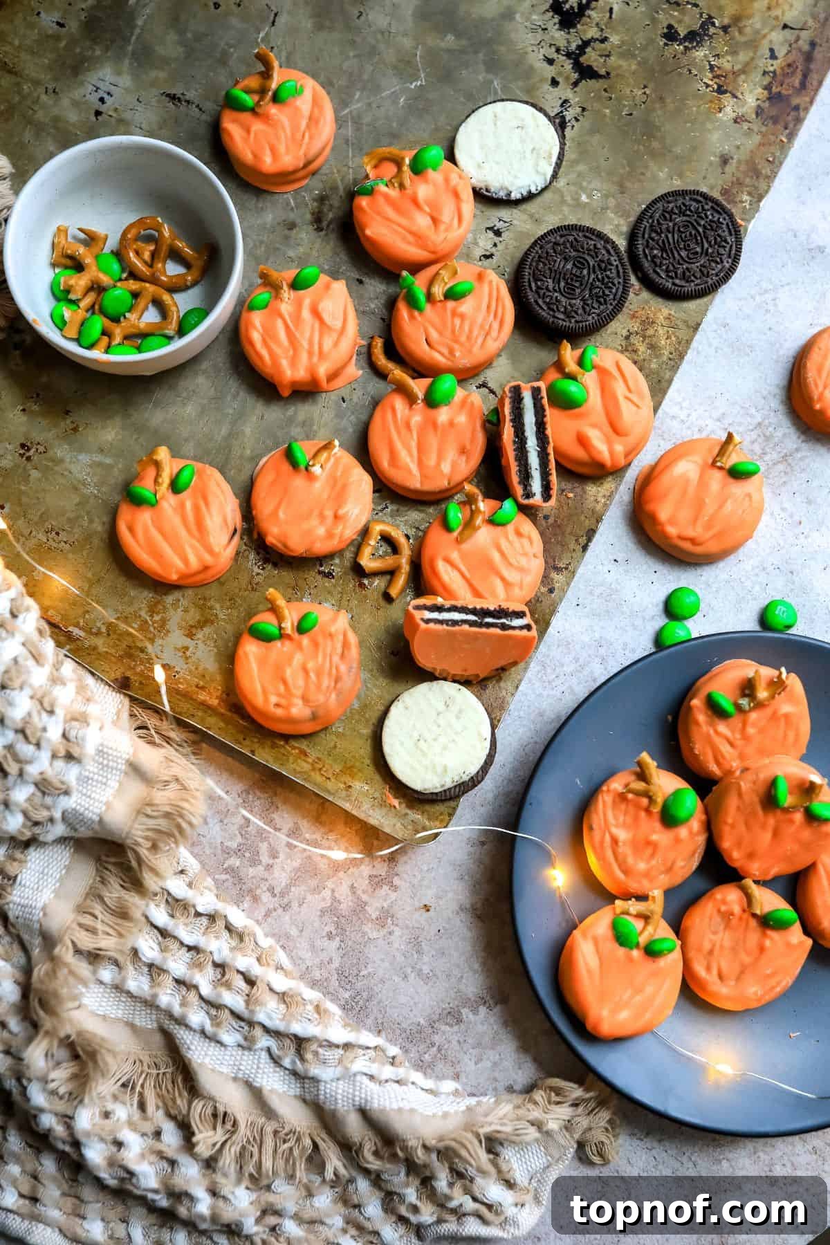 A cookie sheet filled with freshly decorated pumpkin cookies and extra pretzel pieces, ready to be chilled and enjoyed.