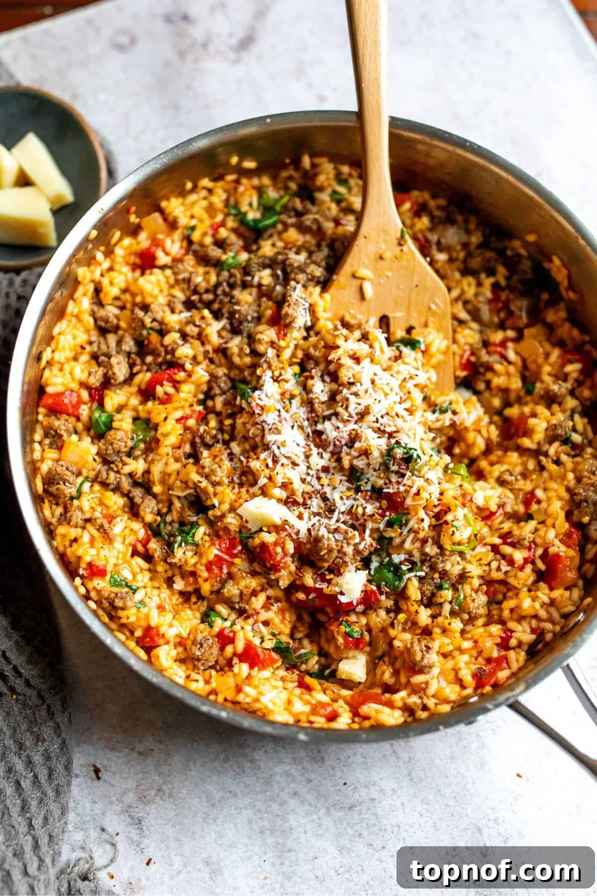 A large skillet brimming with freshly cooked Sausage Risotto, generously topped with grated Parmesan cheese, ready to be served.