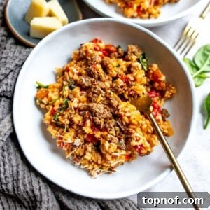 White ceramic bowl with risotto and tomatoes and a gold fork on the side.