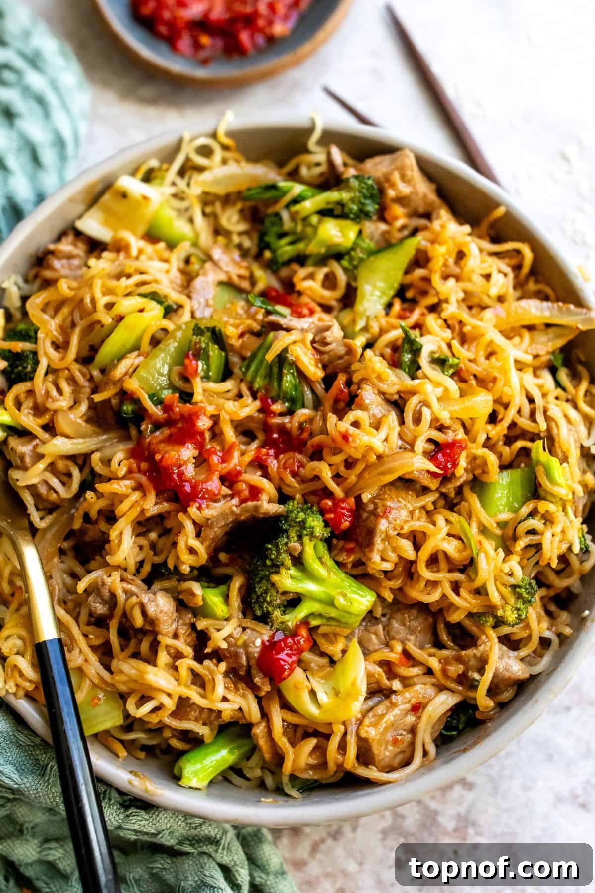 Sizzling Beef and Broccoli Noodles 5 An inviting close-up of Beef and Broccoli Fried Noodles, showcasing the vibrant red sauce, perfectly cooked beef, tender broccoli, and golden-fried noodles. Red pepper flakes are sprinkled on top for garnish.