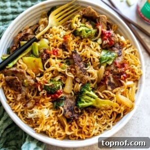 A white bowl filled with golden-brown crispy noodles, succulent beef strips, and vibrant green broccoli florets, coated in a rich, glossy red sauce. A fork is tucked into the side of the noodles.