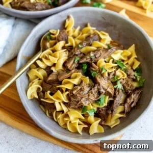 Grey bowls with noodles and beef. A gold spoon on the side with parsley garnish.