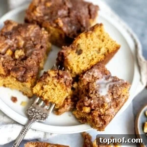A beautifully sliced Apple Cinnamon Cake on a white plate with a silver fork beside it, inviting a taste of its moist texture and crunchy topping.