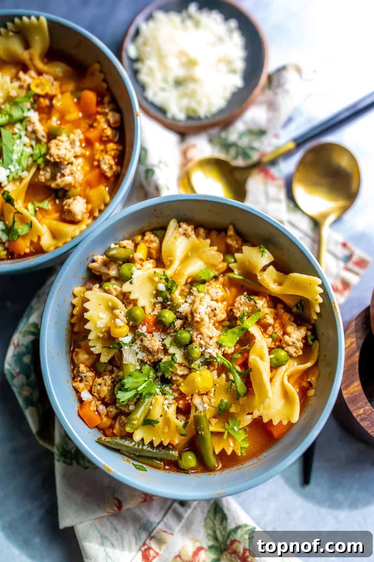Two grey bowls filled with savory ground chicken soup, garnished with fresh herbs, resting on a textured tea cloth, inviting a warm and comforting meal.