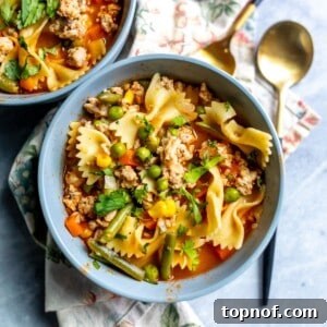 Grey bowl with broth, veggies and ground chicken in it on a tea towel.