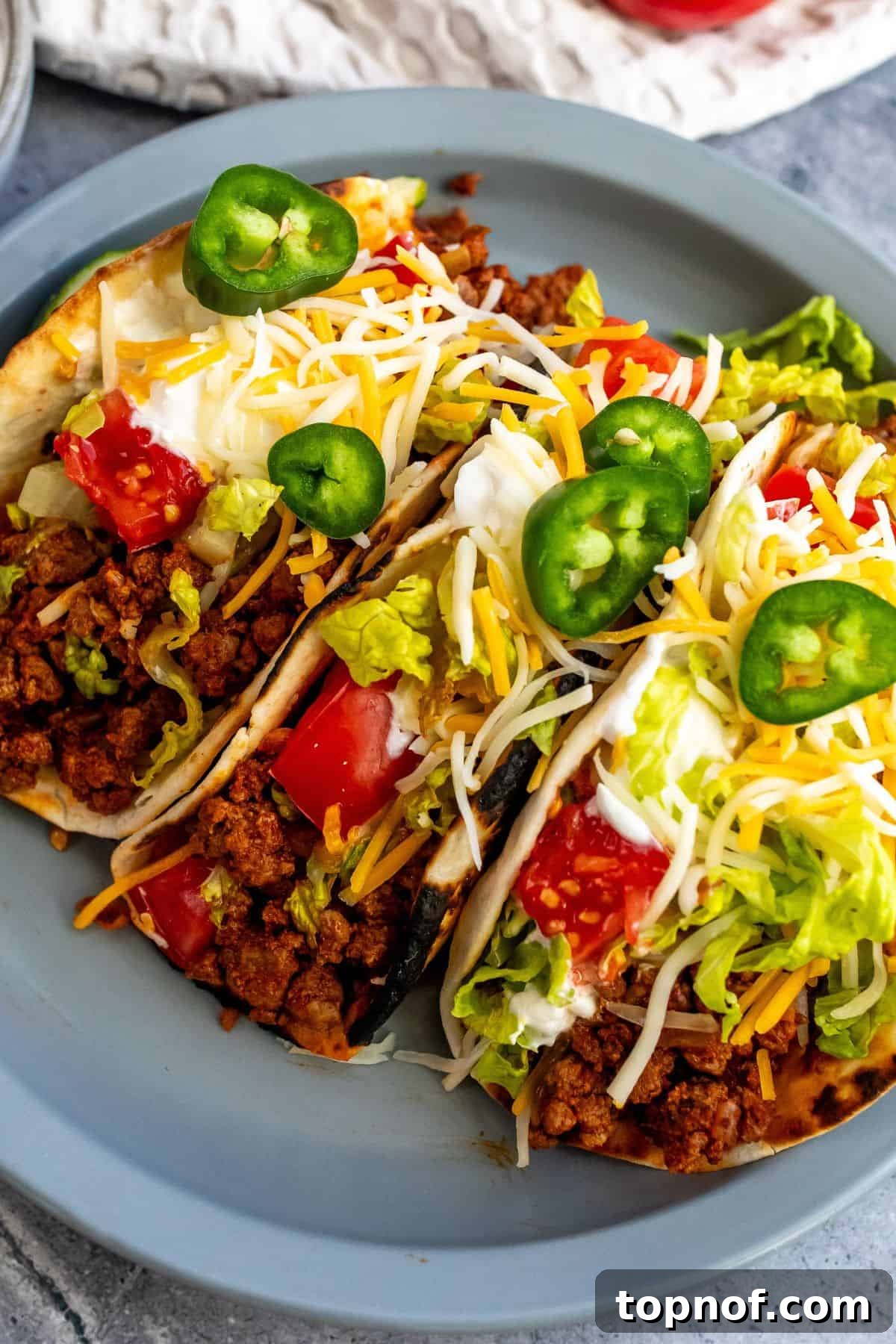 Flavorful Ground Beef Soft Tacos 5 Three beef soft tacos on a plate topped with lettuce, sour cream, cheese, and jalapenos.