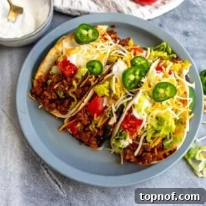 Flavorful Ground Beef Soft Tacos 6 Beef soft tacos on a gray plate with cheese, lettuce, and jalapenos.
