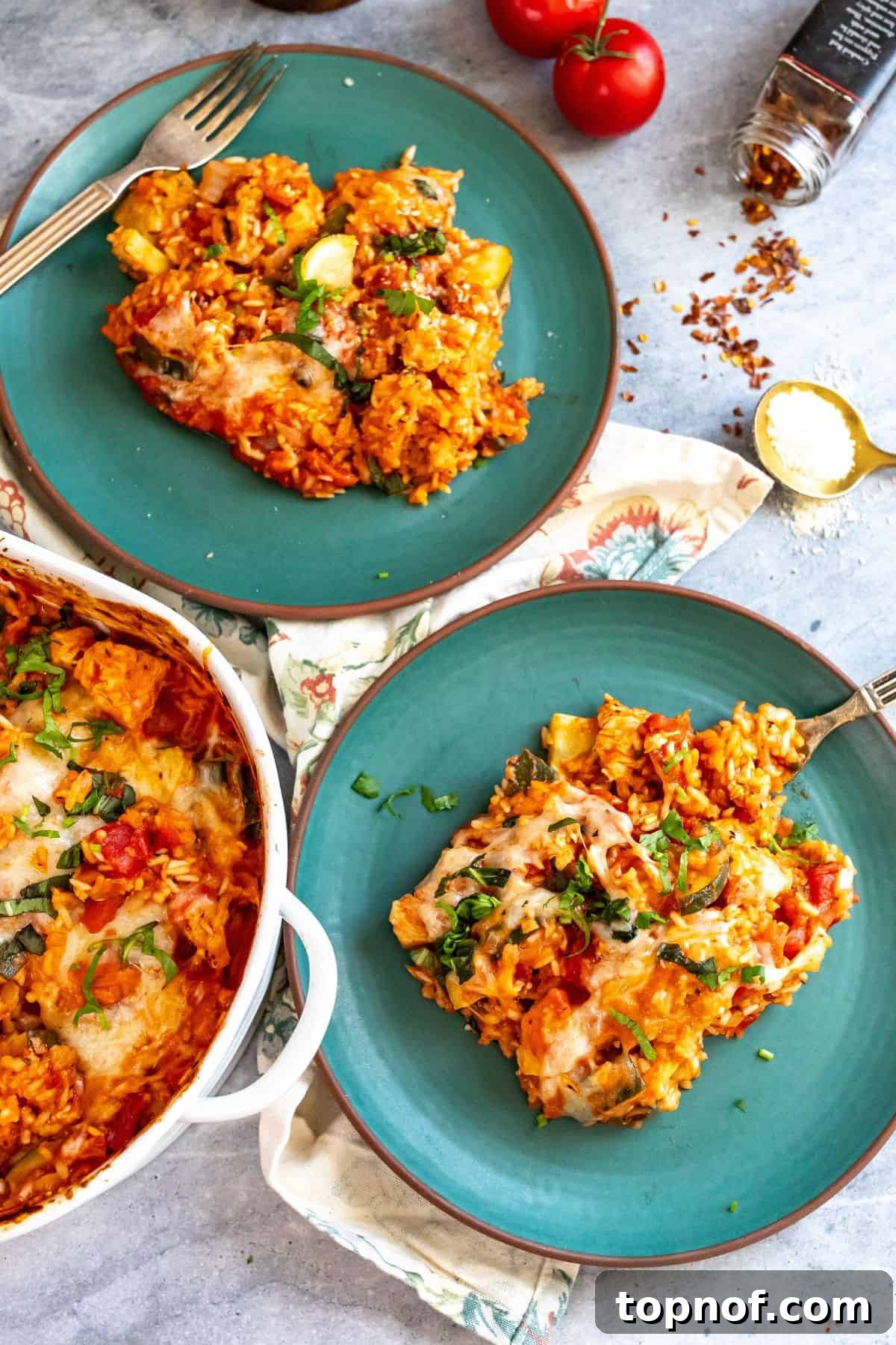Savory Chicken Tomato Bake 2 Green ceramic plates with brown rims. Casserole on the plates garnished in basil and cheese. A large, appetizing portion of chicken and tomato casserole, beautifully garnished with fresh basil leaves and a sprinkle of grated cheese, served on elegant green ceramic plates with earthy brown rims. The casserole features tender chicken pieces, fluffy rice, and a rich, inviting tomato sauce.
