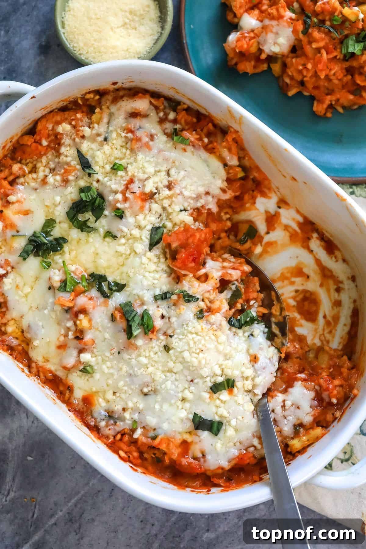 Savory Chicken Tomato Bake 5 White casserole dish filled with rice and chicken covered in cheese. A pristine white casserole dish, generously filled with a delectable mix of fluffy rice and tender chicken, all blanketed under a rich, melted layer of golden-brown cheese, ready to be served.