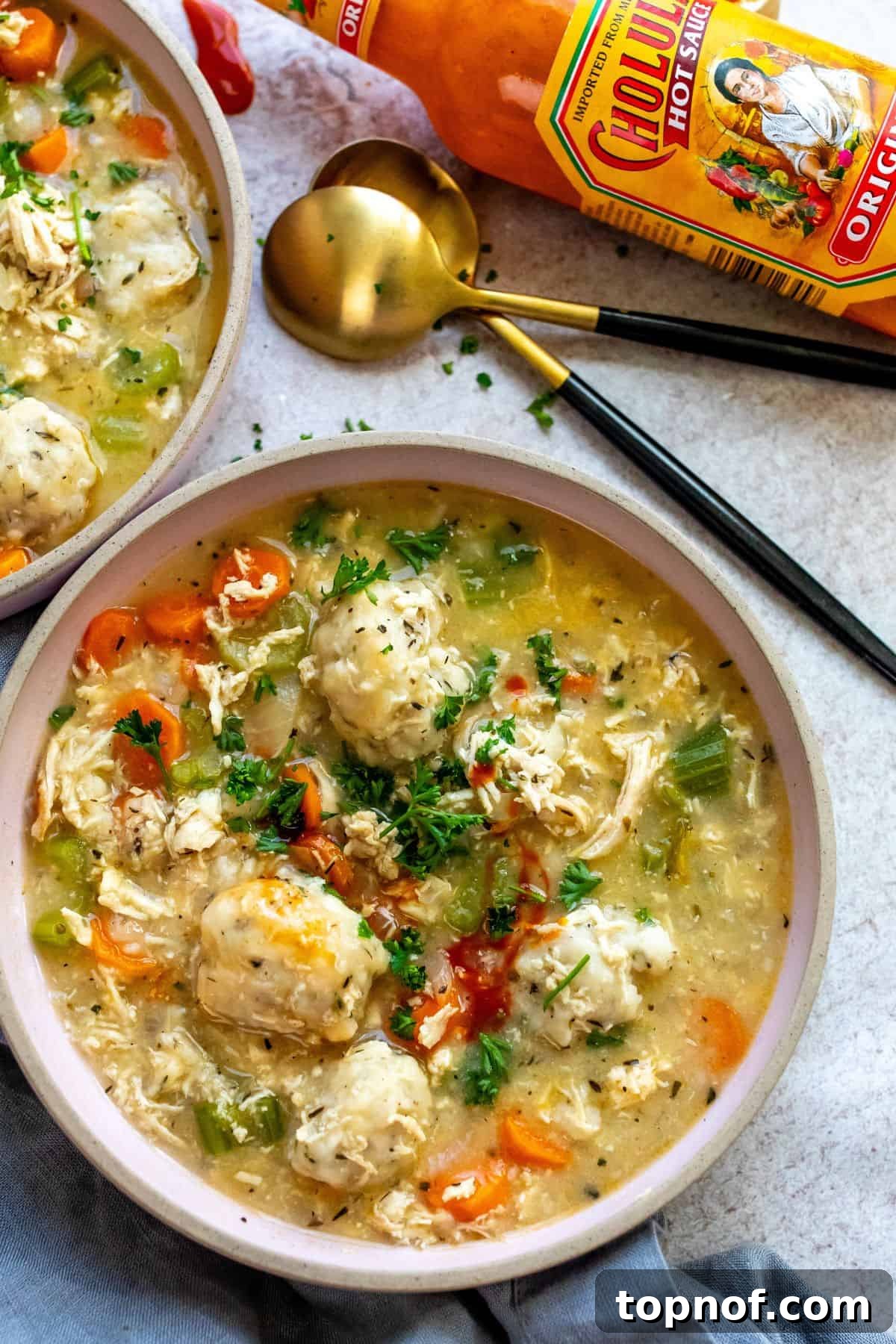 Pink ceramic bowls filled with creamy chicken and dumpling soup, with a black and gold spoon resting on the side, inviting a warm, comforting meal.