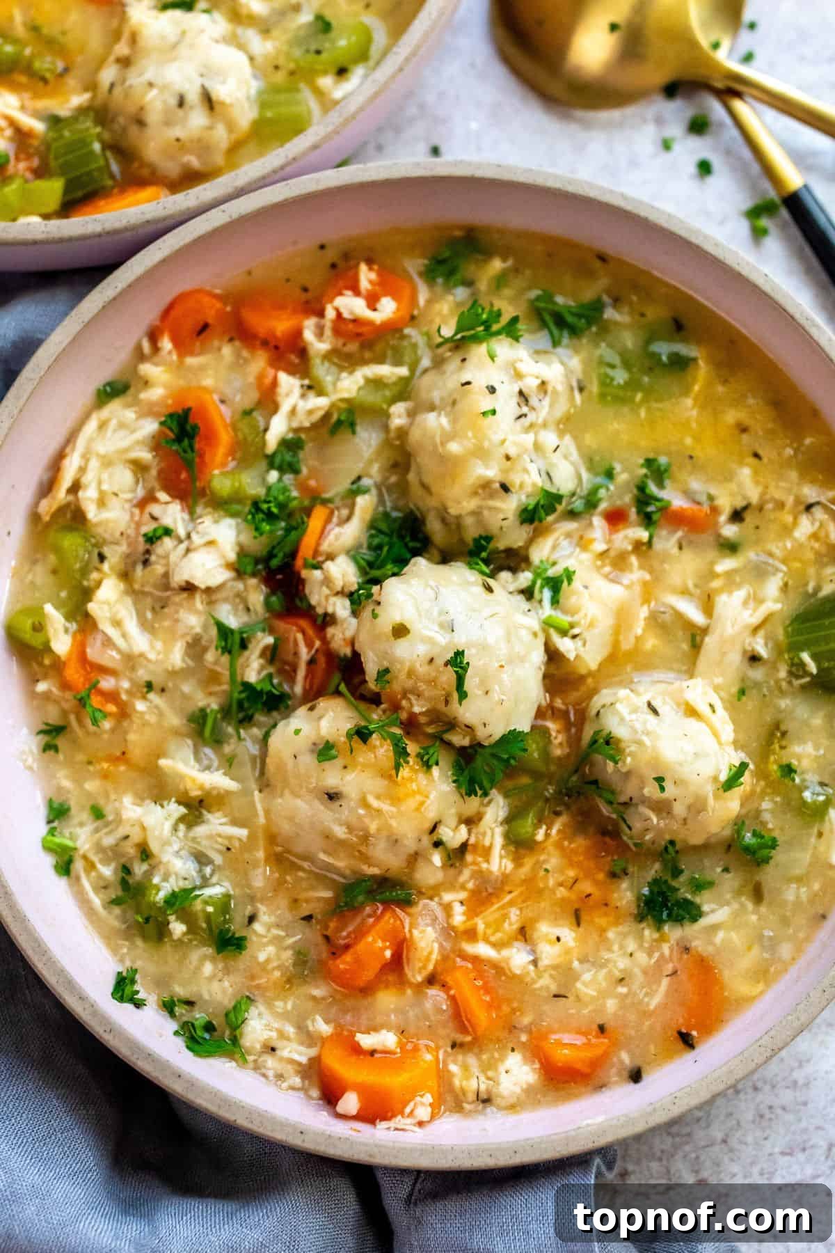 Pink ceramic bowls filled with steaming creamy chicken and dumpling soup, ready to be served, with a black and gold spoon off to the side, emphasizing comfort and warmth.