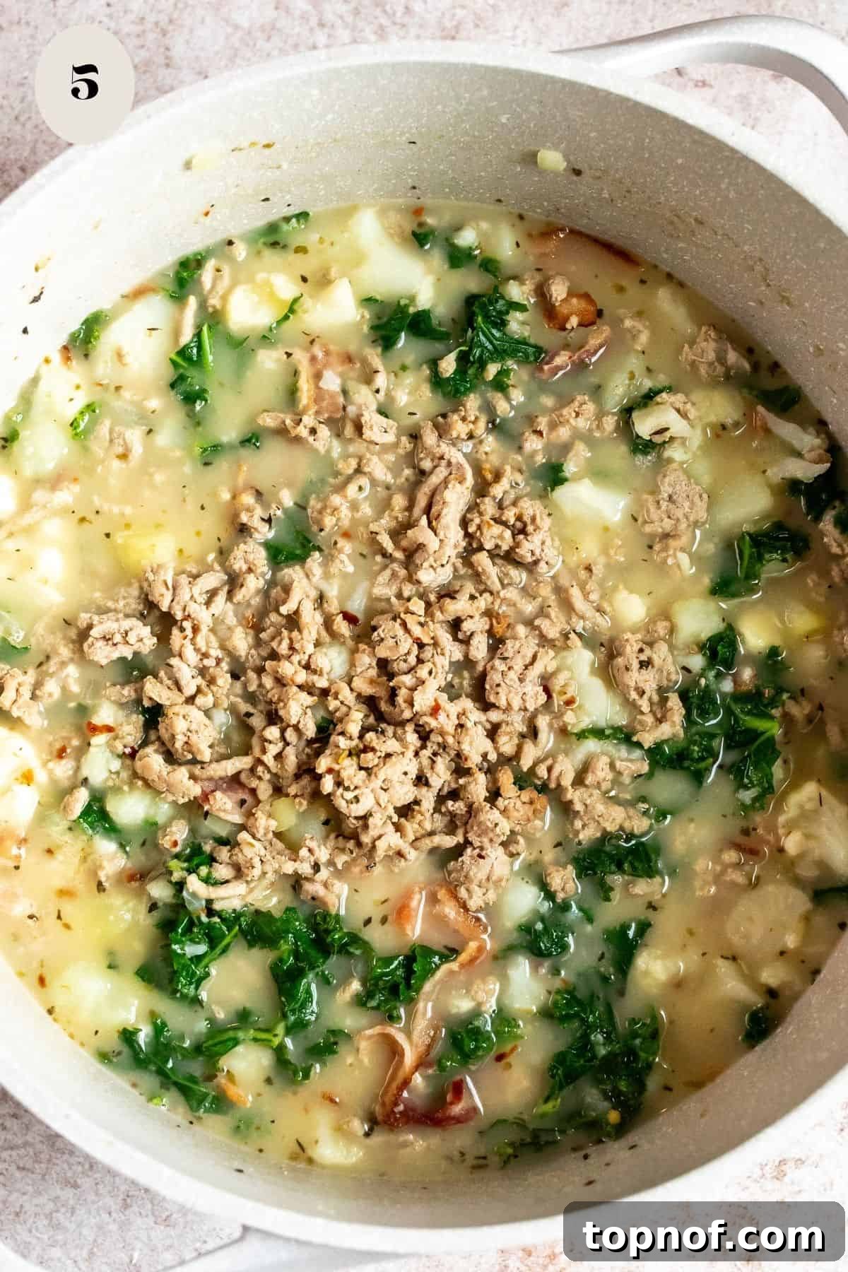 Slimmed-Down Slow Cooker Zuppa Toscana 5 A close-up shot of creamy Zuppa Toscana soup in a grey bowl, garnished with crispy bacon and parsley, ready to be enjoyed.