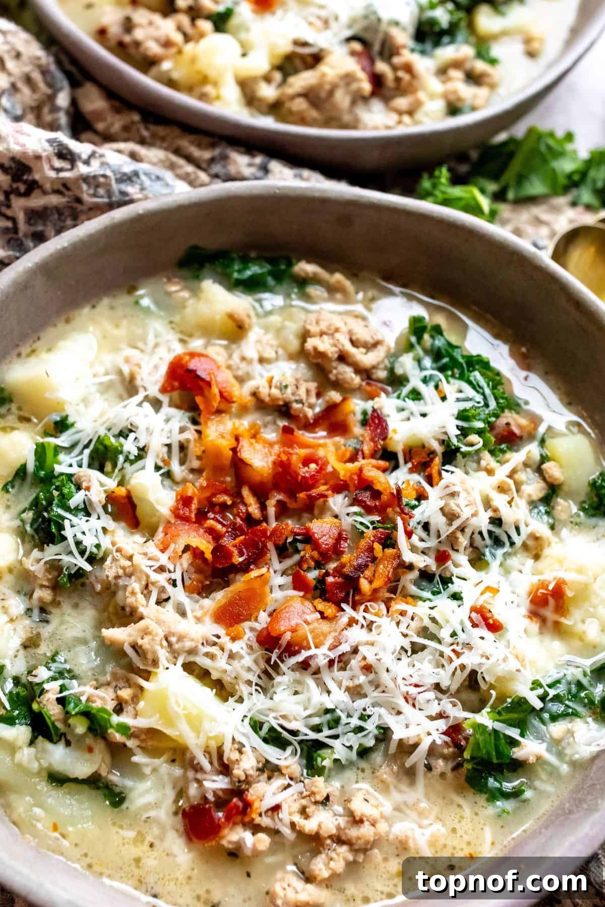 Slimmed-Down Slow Cooker Zuppa Toscana 6 Close-up of a serving of healthy Zuppa Toscana in a grey pottery bowl, garnished with crispy bacon bits, fresh parsley, and a gold spoon resting beside it.
