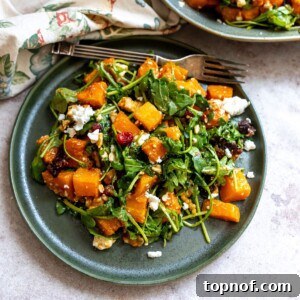 Green plate with salad and roasted butternut squash on it. Silver fork on the side.