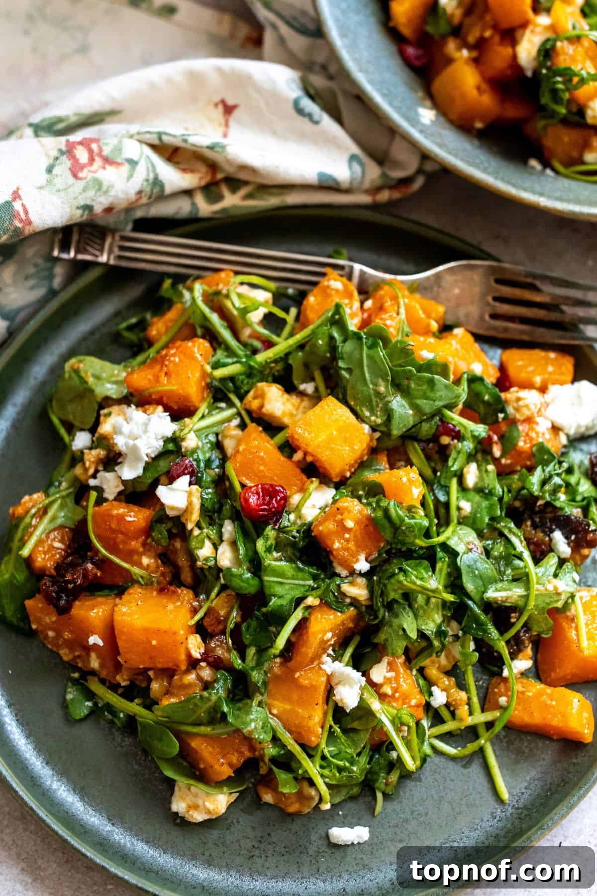 Green plate with a vibrant Butternut Squash Feta Salad on it. A silver fork rests on the side.