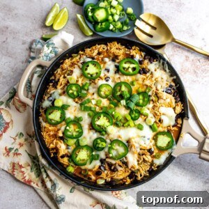 Skillet filled with chicken and cheese and jalapeños on top. Gold serving spoon on the side.