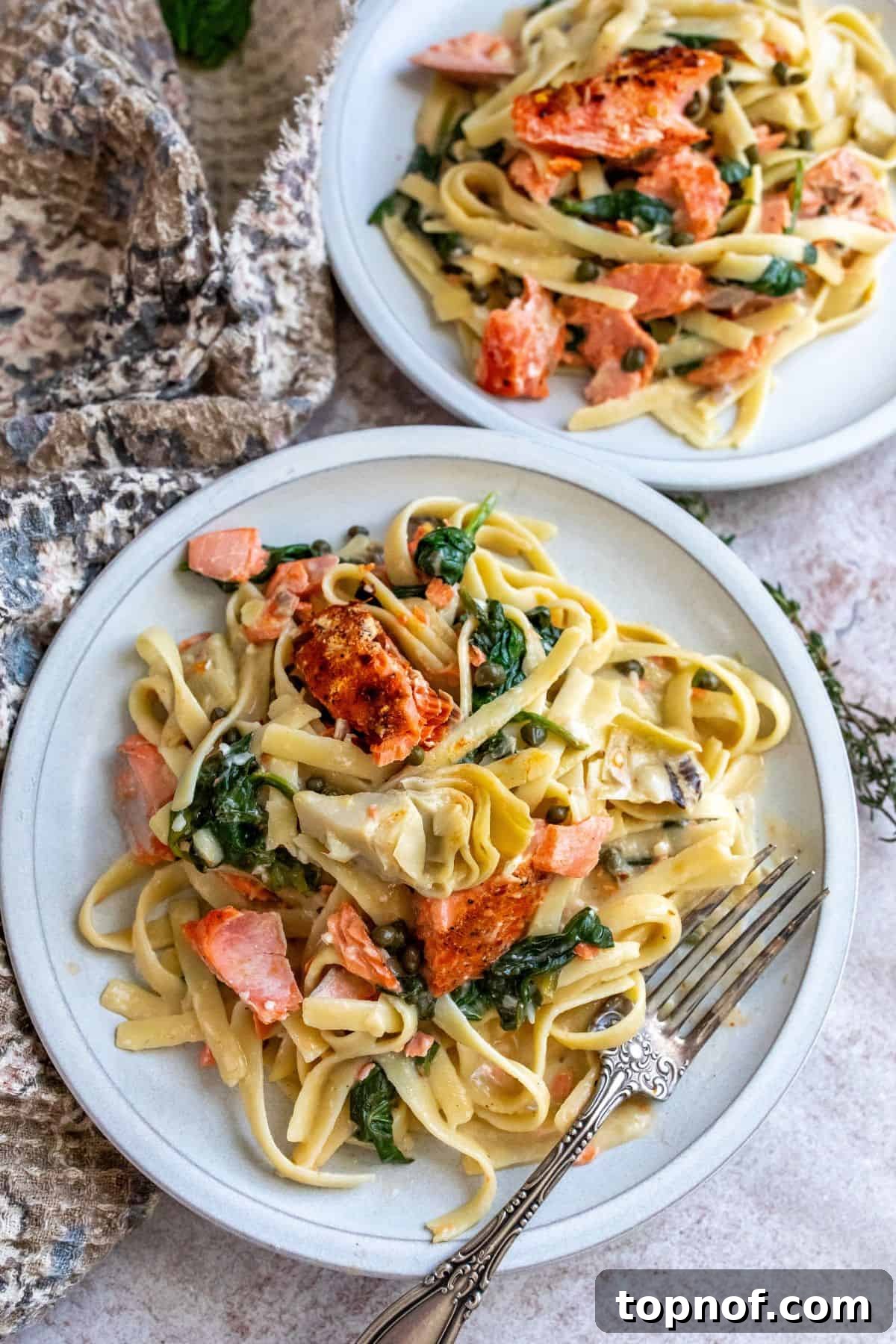Lemon Herb Salmon Pasta Bake 2 White ceramic plate with pasta, cream sauce and salmon. A silver fork on the side.