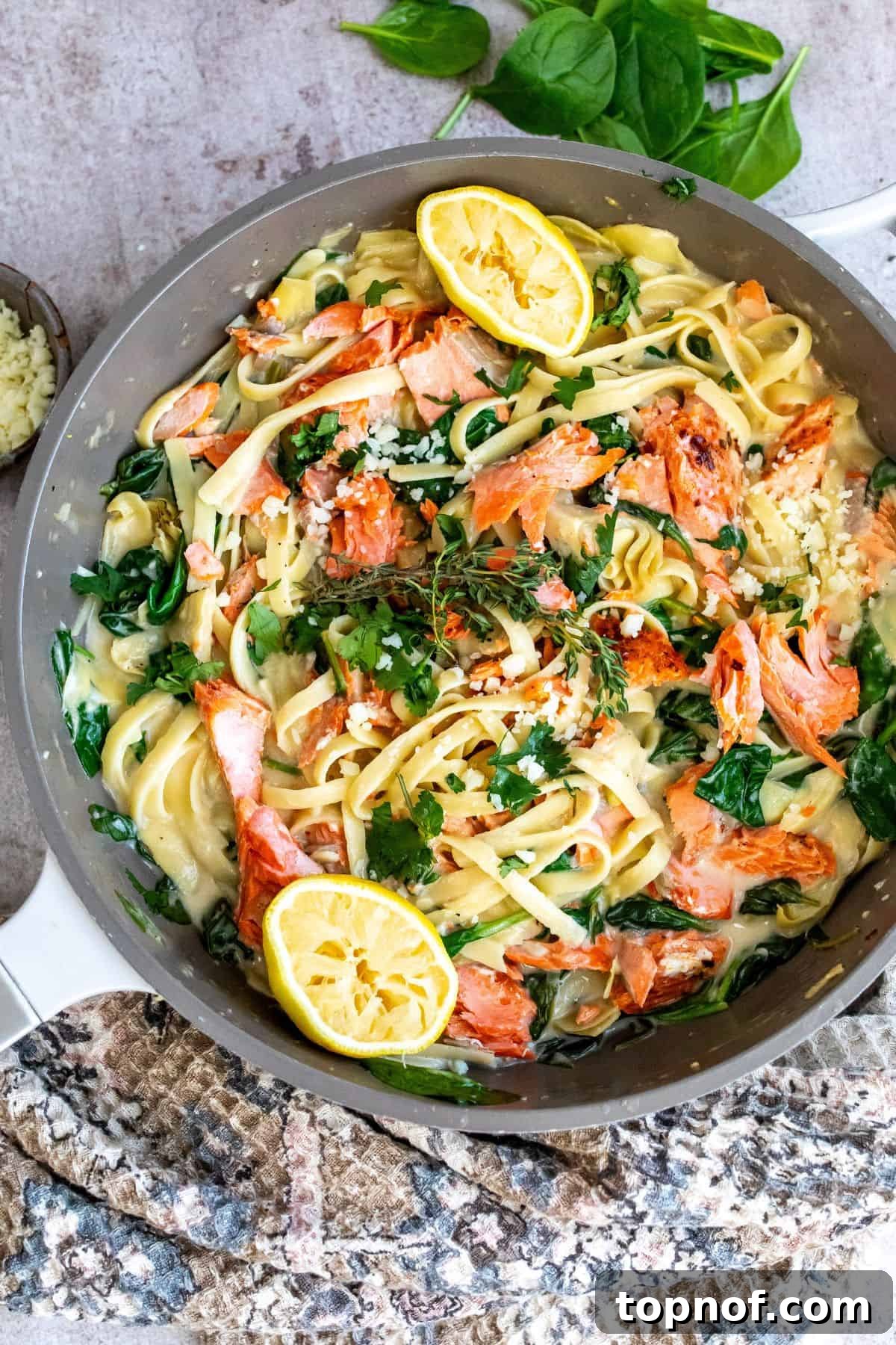 Lemon Herb Salmon Pasta Bake 5 Grey skillet with pasta and cream sauce. Lemons and salmon on top.