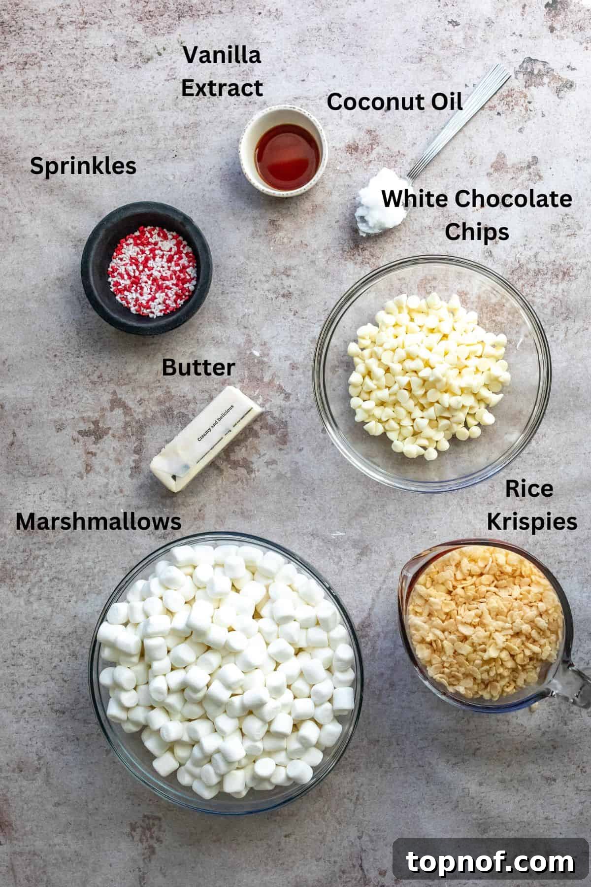 Arrangement of key ingredients for Christmas Rice Krispies treats, including mini marshmallows, rice cereal, white chocolate chips, and coconut oil, neatly displayed on a rustic surface, ready for preparation.