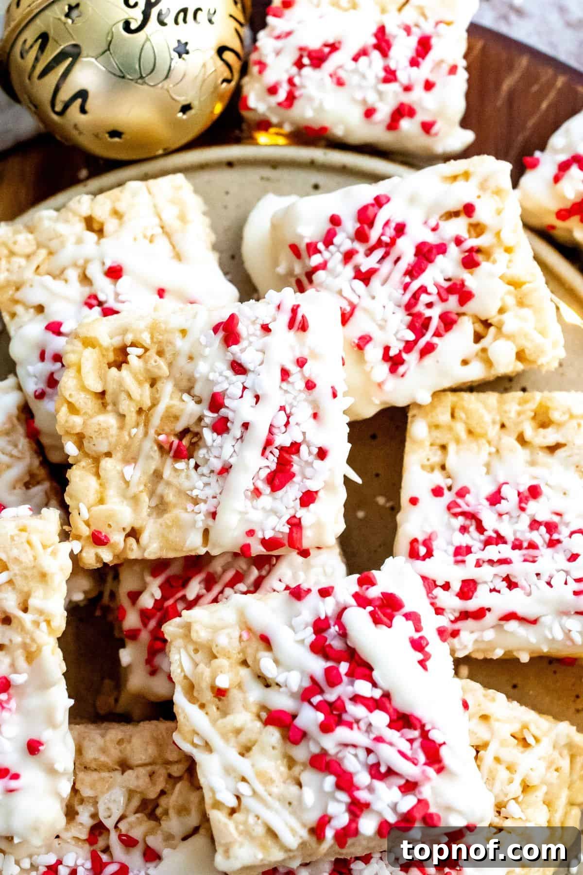 A close-up shot of a perfectly decorated Christmas Rice Krispie Treat, adorned with colorful holiday sprinkles, next to a shimmering gold ball, highlighting the festive details and inviting texture.