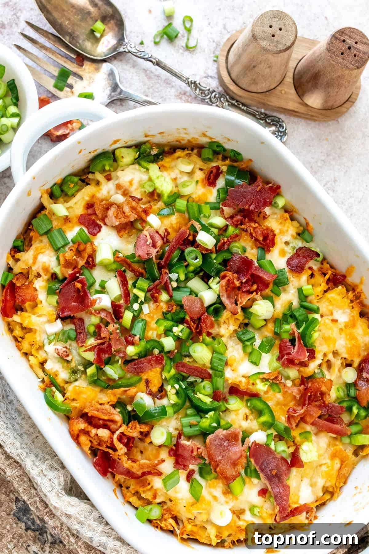 Hearty Chicken Hash Brown Bake 2 A large white casserole dish filled with golden-brown chicken and jalapeño casserole, generously topped with melted, bubbly cheese and fresh green onions as garnish.