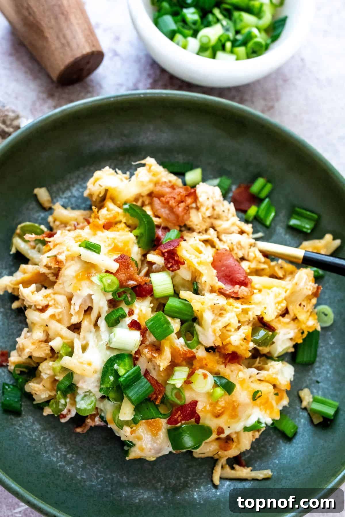 Hearty Chicken Hash Brown Bake 5 A vibrant green bowl filled with a generous serving of Jalapeño Popper Chicken and Hash Brown Casserole, beautifully topped with melted cheese, crispy bacon, and fresh herbs, ready for eating.