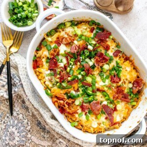 A top-down view of a white casserole dish filled with golden-brown chicken and hash brown casserole, generously topped with melted cheese and vibrant green jalapeño slices, ready for serving.