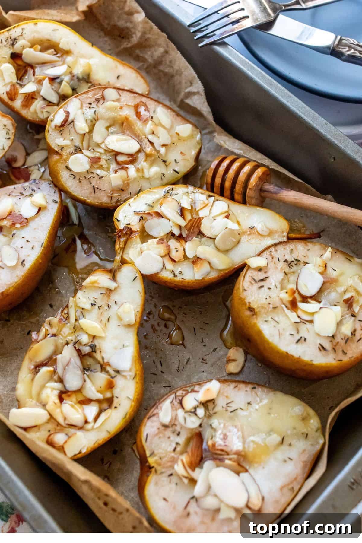 Sweet and Savory Brie Baked Pears 2 Golden-brown baked pear halves adorned with melted brie, toasted almonds, and a glistening honey drizzle, artfully arranged on brown parchment paper with a side of honey and small plates, ready to be served.